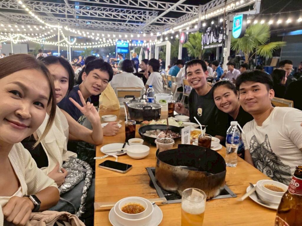 Japanese exchange student Haruma eating Mookata with his Thai host family at an outdoor restaurant