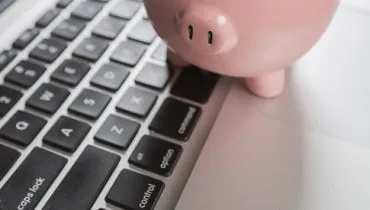 Piggy Bank Resting on Laptop Computer Keyboard.