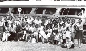 Black and white photo of students posing in front of a bus.