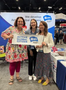 Two AFS Intercultural Programs representatives and a conference attendee hold an "Active Global Citizen" sign at the AFS booth during the NAFSA 2026 Annual Conference & Expo.