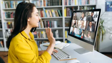 Online education. A female student learning online at home, she waving hand to other students or colleagues on computer monitor in video conference and smiling