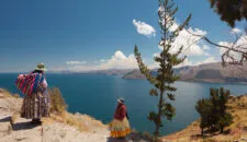 Two Women In Traditional Bolivian Clothes Standing On The Rock Close To The Titicaca Lake.