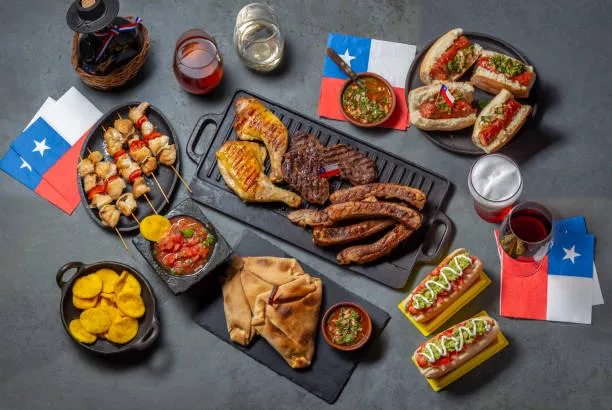 Chilean independence day table with traditional festive food for fiestas patrias. Asado bbq, choripan, empanadas, anticuchos, sopaipillas, completos, salsas, wine, mote and coctail terremoto. Dish and drink on 18 September party